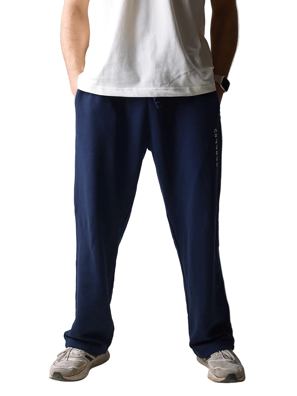 A person wearing navy blue sweatpants with a vertical white logo on the side, paired with a white t-shirt and beige sneakers, standing against a light gray studio background.