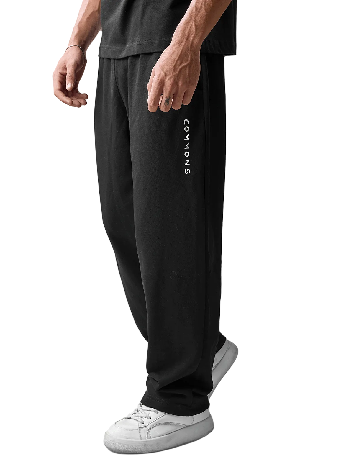 A person wearing black wide-leg sweatpants with vertical white 'CANYONS' branding on the left leg, paired with white sneakers, photographed against a light gray studio background.
