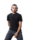 A man wearing a black short-sleeve crewneck t-shirt and dark gray sweatpants, sitting against a light gray studio background.