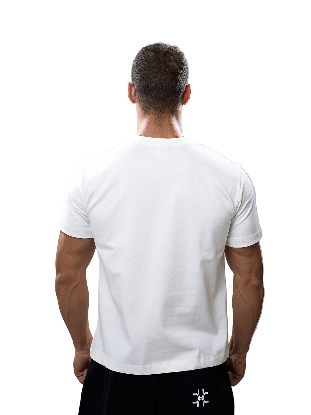 A man viewed from behind wearing a plain white short-sleeve crew-neck t-shirt and black pants against a solid gray studio background.
