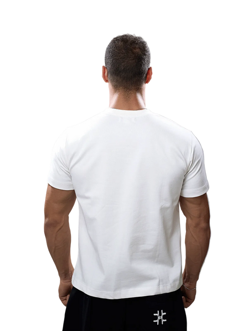 A man viewed from behind wearing a plain white short-sleeve crew-neck t-shirt and black pants against a solid gray studio background.