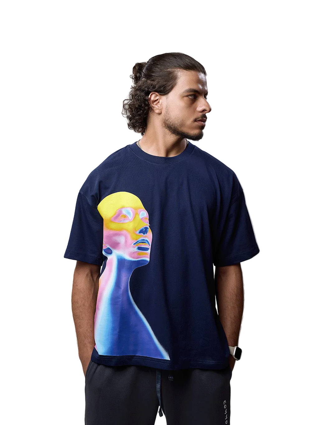 A man wearing a navy blue t-shirt with a colorful graphic print of a stylized face in yellow, pink, and blue, paired with dark gray sweatpants, photographed against a neutral gray background.