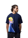 A man wearing a navy blue t-shirt with a colorful graphic print of a stylized face in yellow, pink, and blue, paired with dark gray sweatpants, photographed against a neutral gray background.