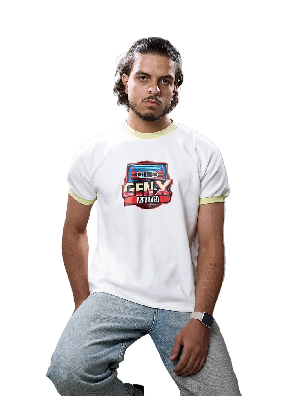 A man wearing a white ringer t-shirt with light yellow trim and a 'GENX APPROVED' cassette graphic on the chest, paired with light blue jeans, sitting on a wooden stool against a gray studio background.