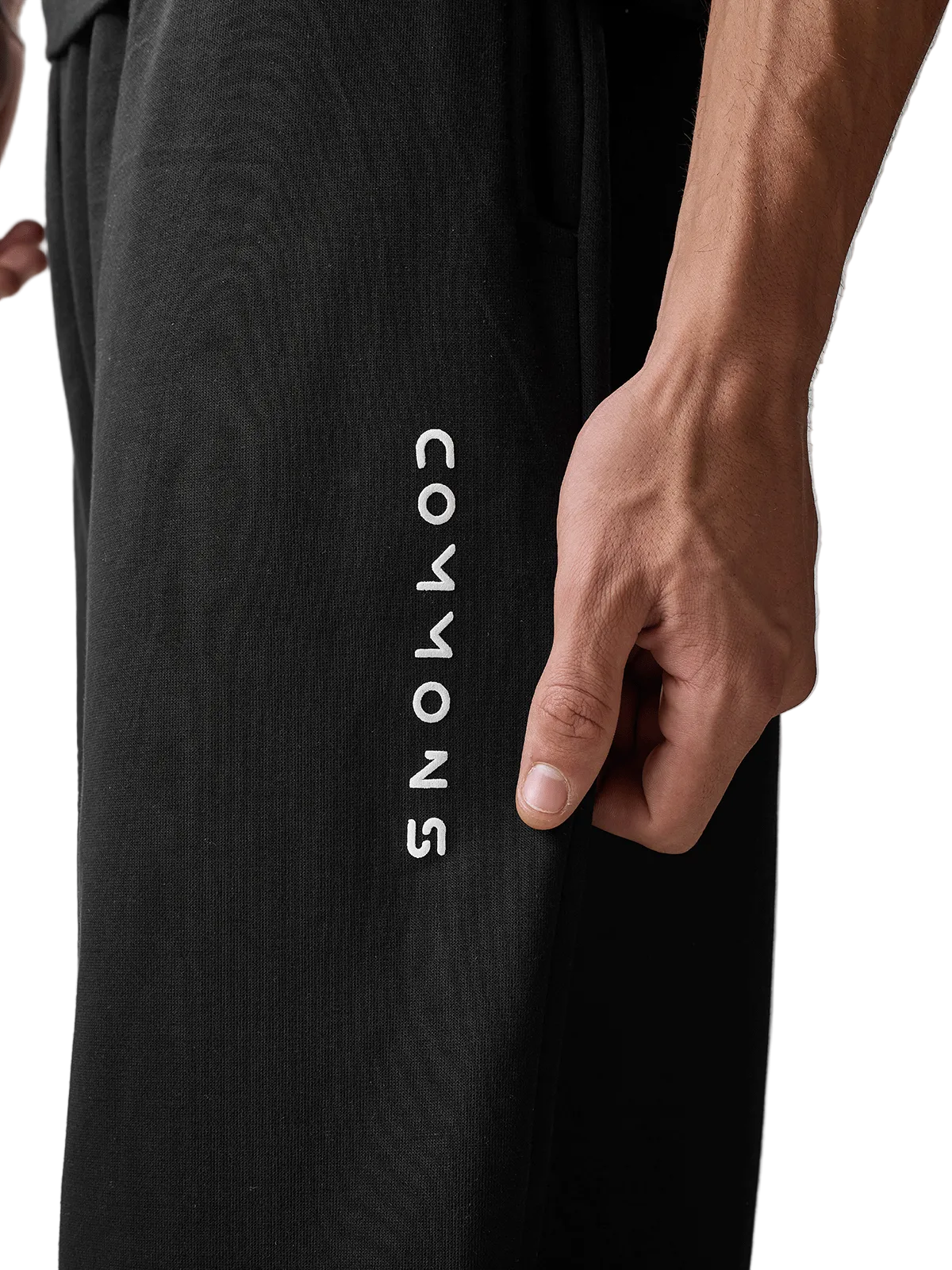 Close-up of a person wearing black wide-leg sweatpants with the brand name 'COWYONS' printed vertically in white on the left leg, against a light gray studio background.