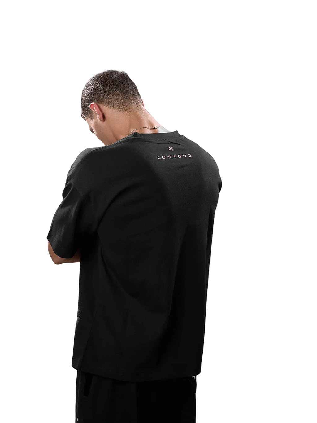 A man viewed from behind wearing a black short-sleeve t-shirt with a small gold 'CANNONS' logo printed on the upper back, set against a solid gray studio background.