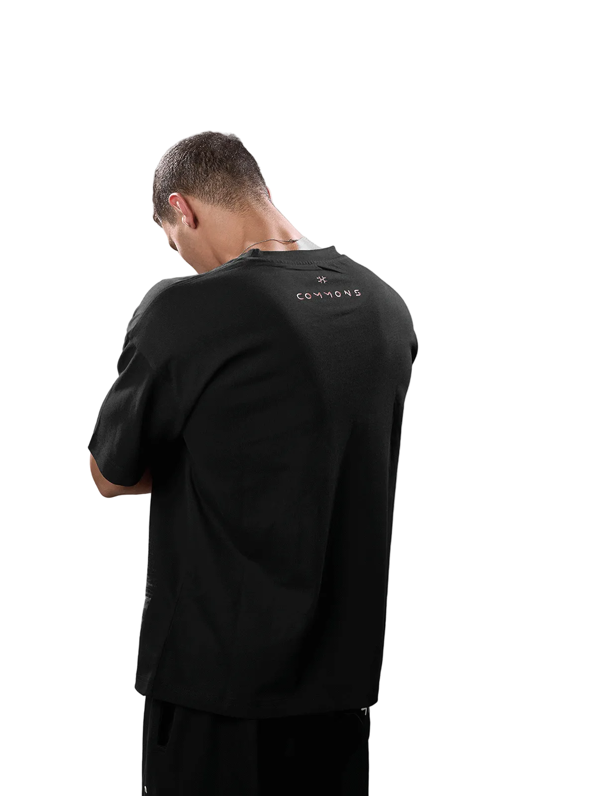 A man viewed from behind wearing a black short-sleeve t-shirt with a small gold 'CANNONS' logo printed on the upper back, set against a solid gray studio background.