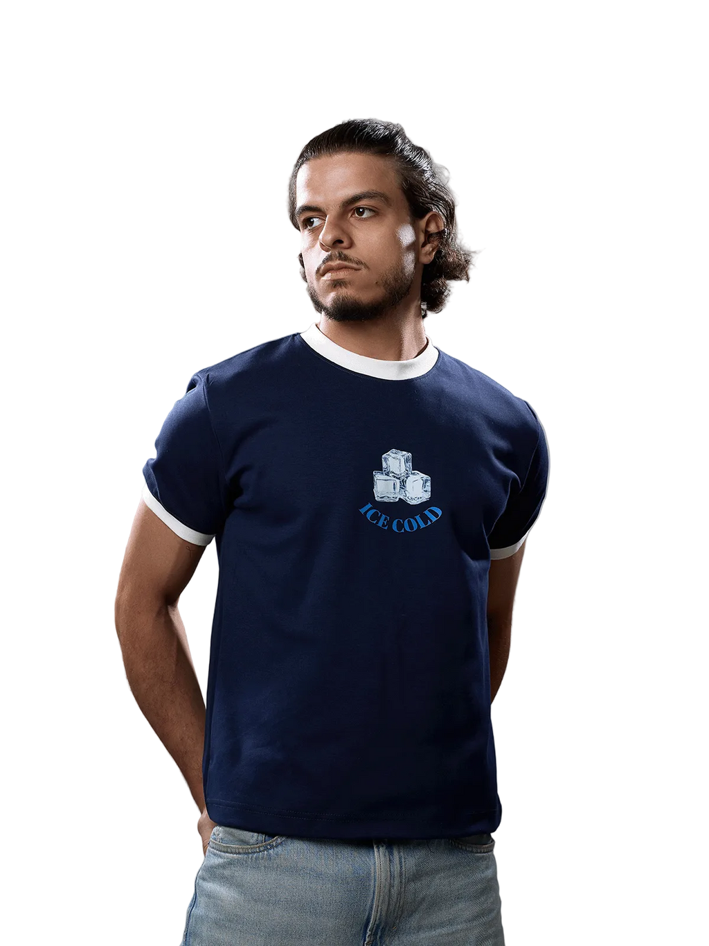 A man wearing a navy blue ringer t-shirt with white trim and a graphic of three ice cubes and the text 'ICE COLD' on the chest, paired with light blue jeans, against a solid gray background.