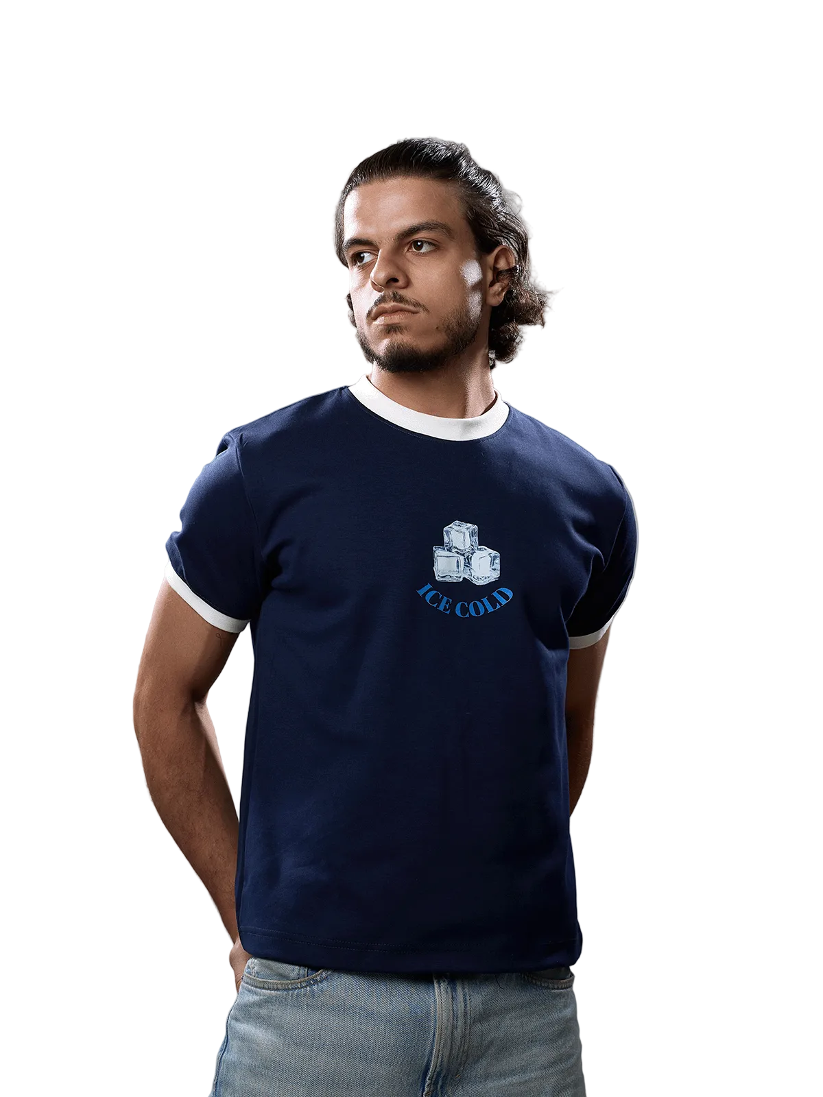 A man wearing a navy blue ringer t-shirt with white trim and a graphic of three ice cubes and the text 'ICE COLD' on the chest, paired with light blue jeans, against a solid gray background.